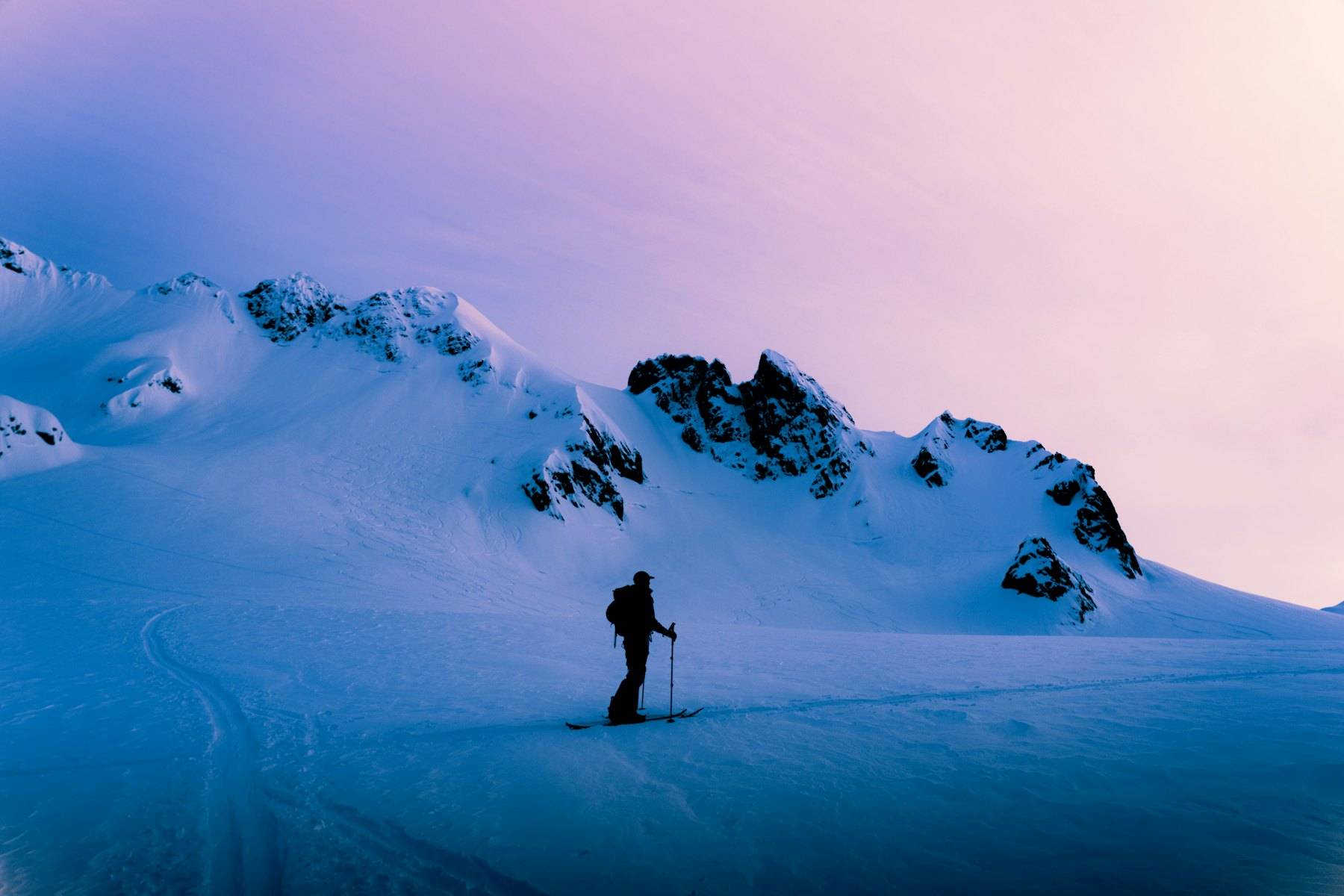 Skier climbing a snow slope under a violet twilight sky