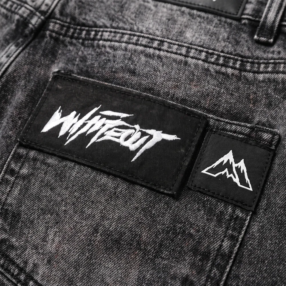 Black WHITEOUT brush-script patch beside a woven twin-peak patch on washed charcoal fabric
