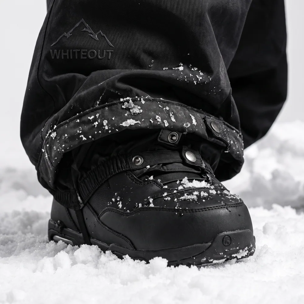 Pant hem with inner gaiter over a black snowboard boot in snow