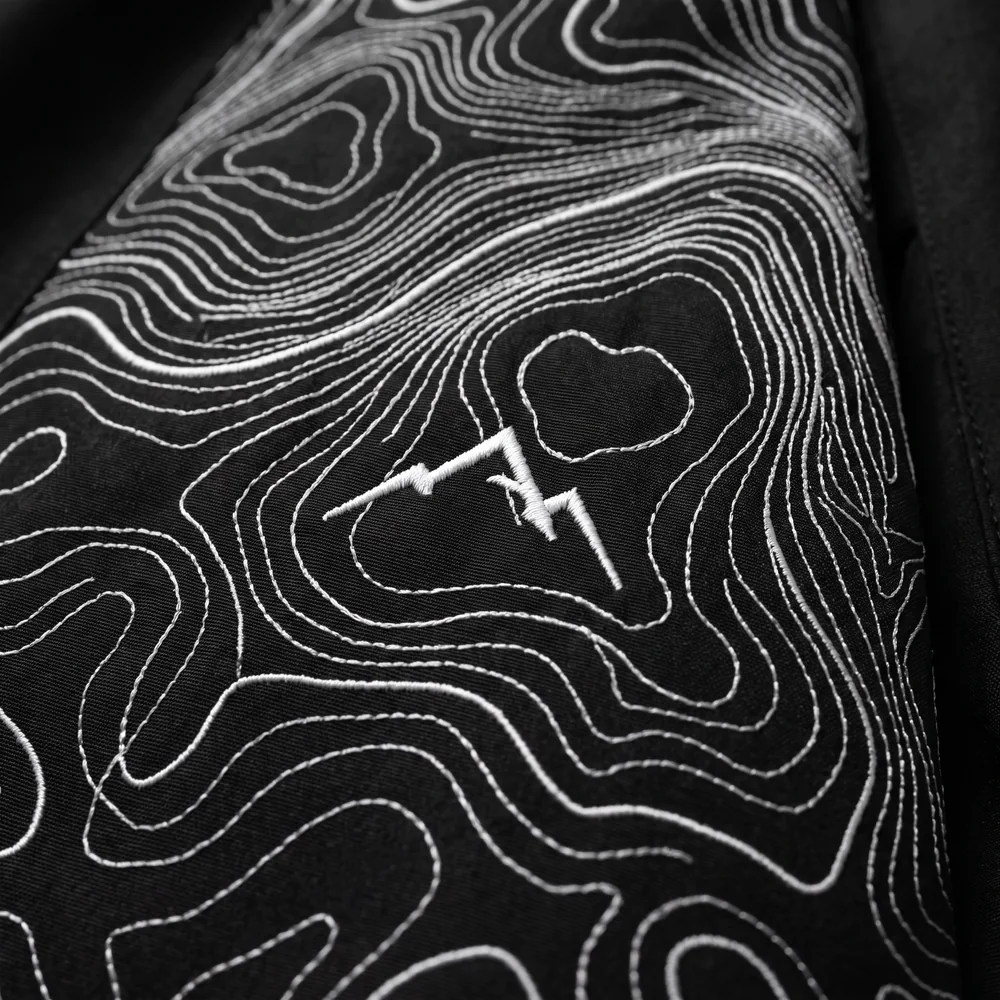 White topographic contour embroidery with a twin-peak emblem on black fabric
